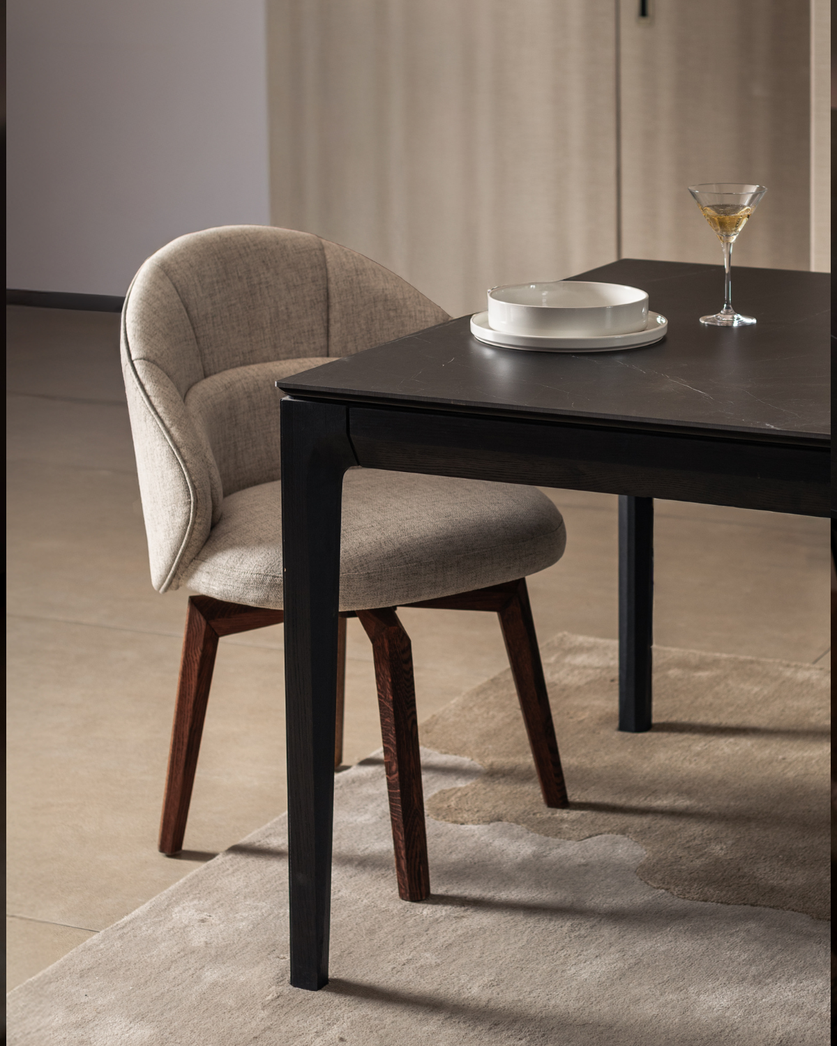 Dining chair next to a dark wooden table with a glass and plates on a neutral background