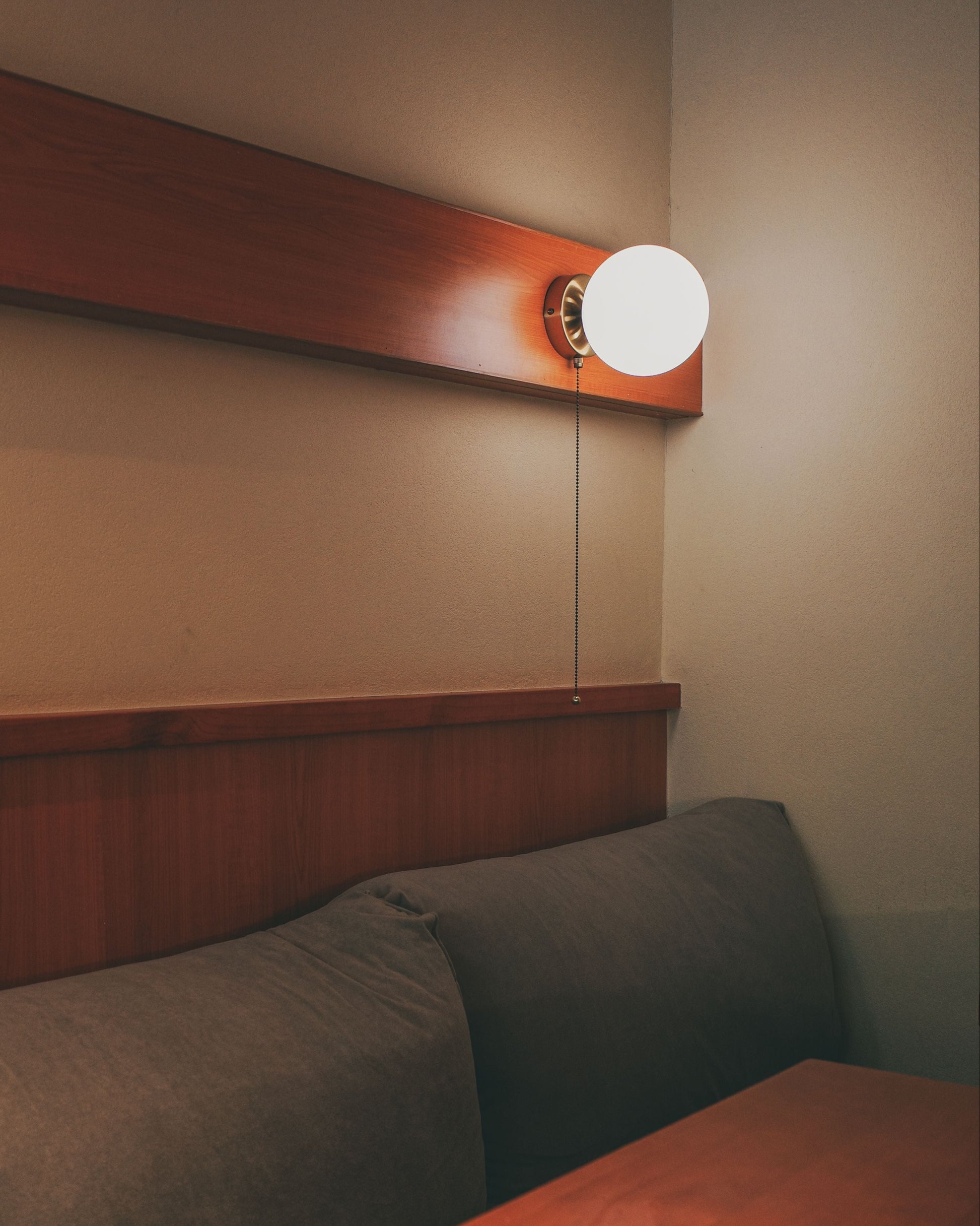 Corner of a room with a wooden bench, cushioned seat, and wall-mounted light fixture.